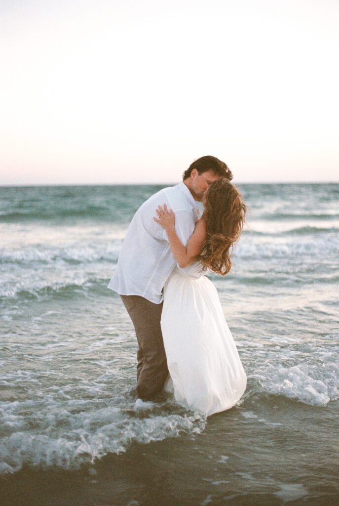 Engaged couple embracing in the ocean during sunset at their romantic Gulf Shores beach engagement session.
