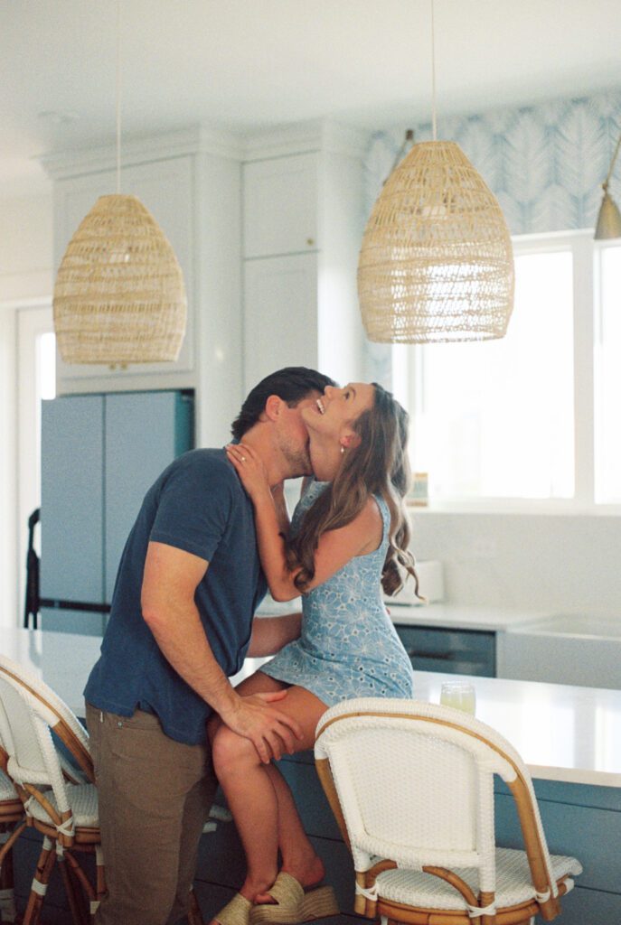 Couple laughing together in a coastal kitchen during their Gulf Shores engagement session at a family beach house in Alabama.