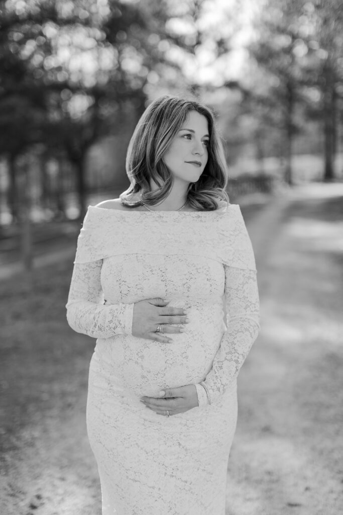 Pregnant mother in a lace maternity gown standing among trees during an outdoor maternity session in Alabama at SpringHouse.