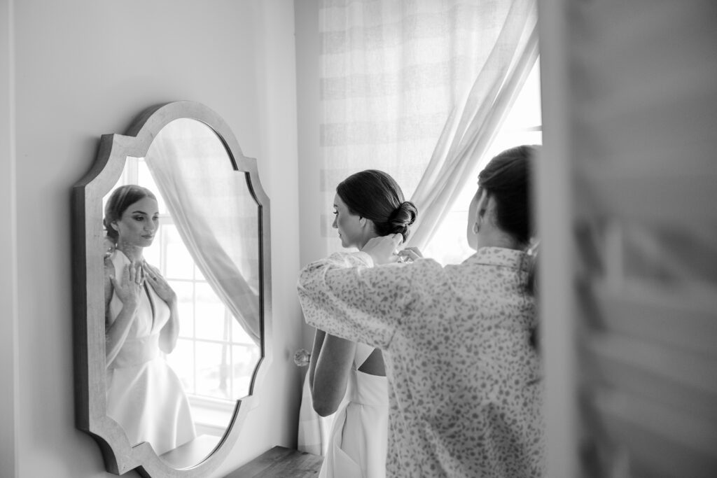 Bridesmaid adjusts Grace’s veil as she looks in the mirror before her wedding