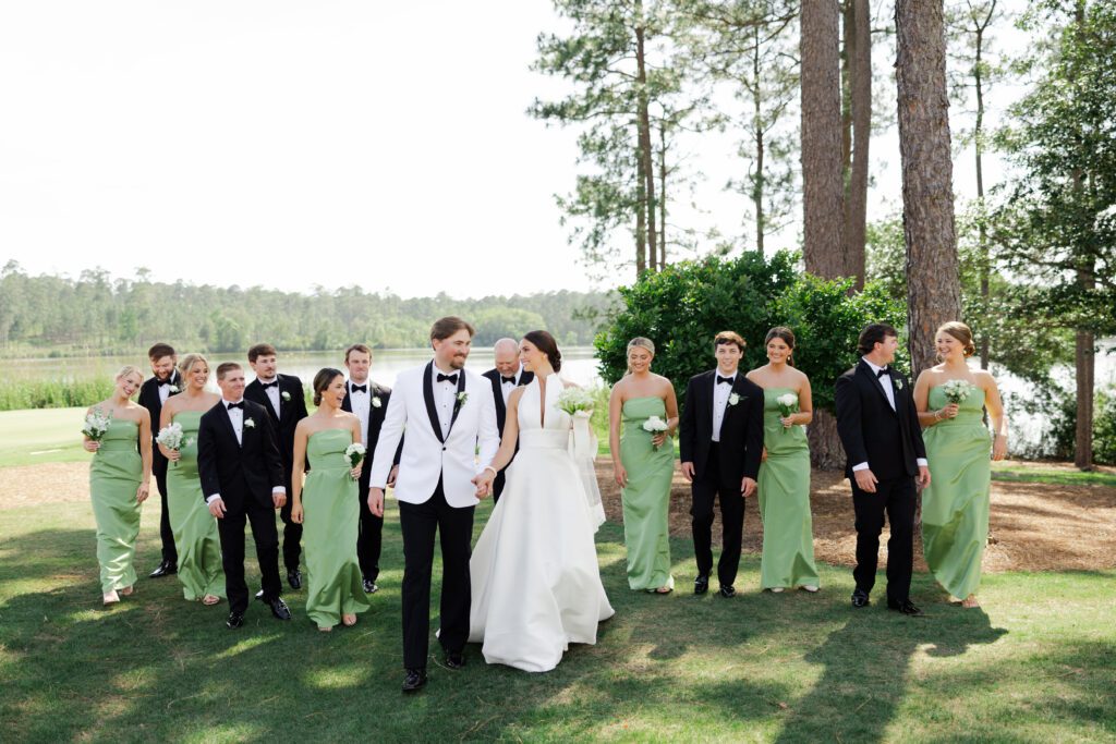 Grace and Lake walk with their wedding party beside the lake at Steelwood Country Club