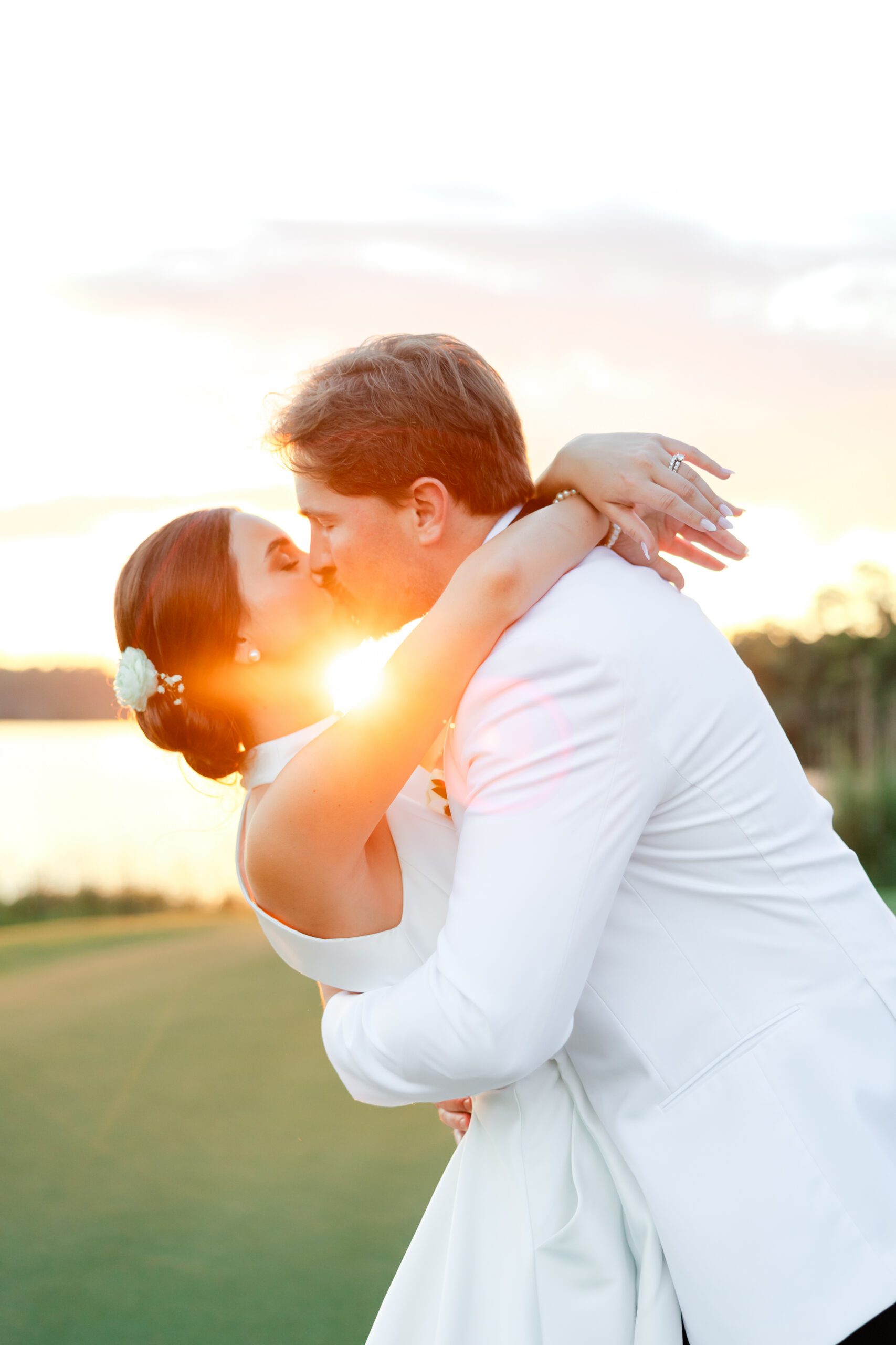 Grace and Lake kiss at sunset beside the lake during their Steelwood Country Club wedding.