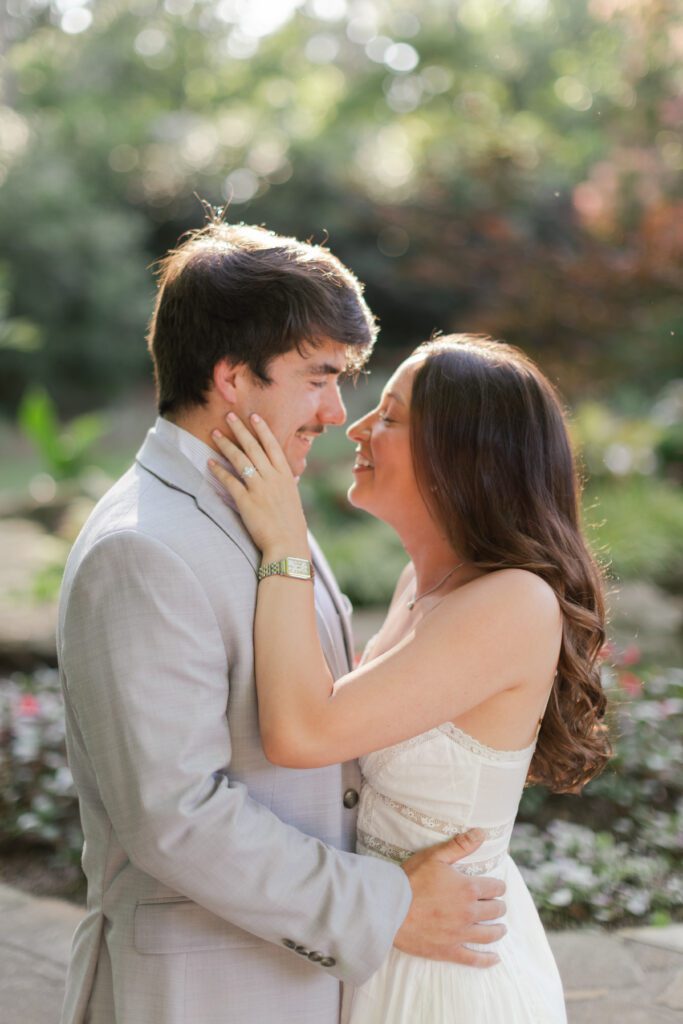 Emily shows her engagement ring while standing close to Brody in the sunlit gardens.