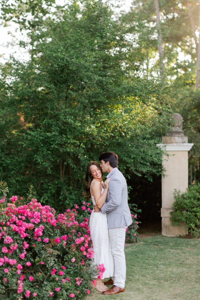 Brody kisses Emily’s forehead beside bright pink roses at Birmingham Botanical Gardens.