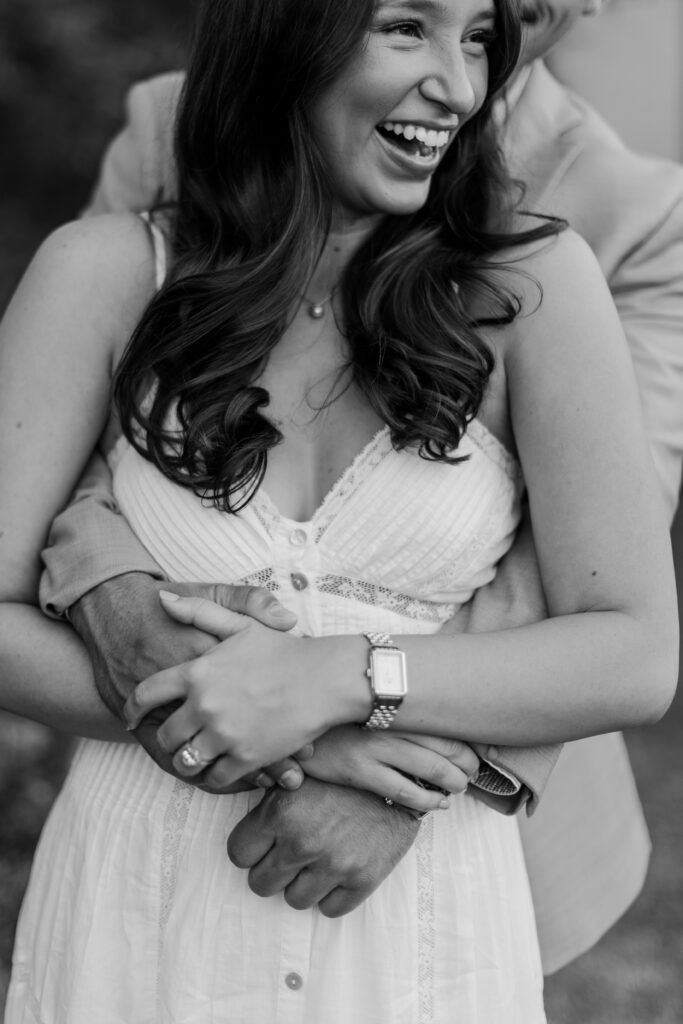 Black-and-white close-up of Emily laughing as Brody wraps his arms around her.