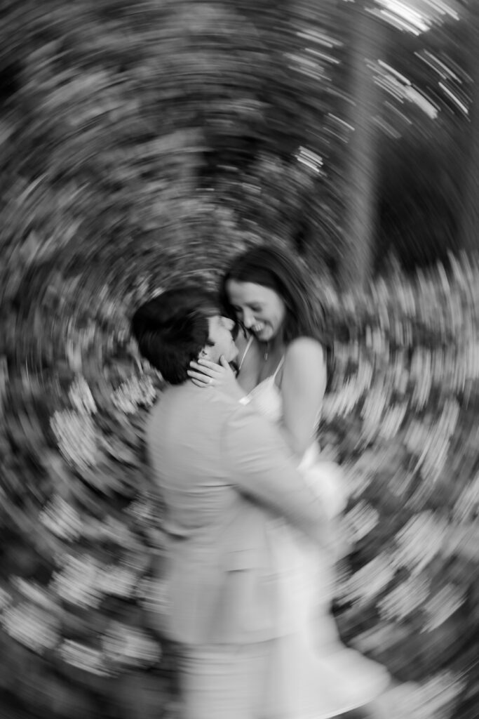 Black-and-white motion blur portrait of Emily and Brody embracing in the gardens.