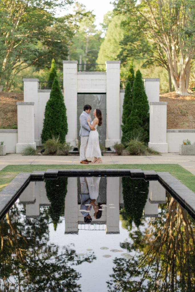 Emily and Brody stand beside a reflecting pool during their Birmingham Botanical Gardens engagement session.