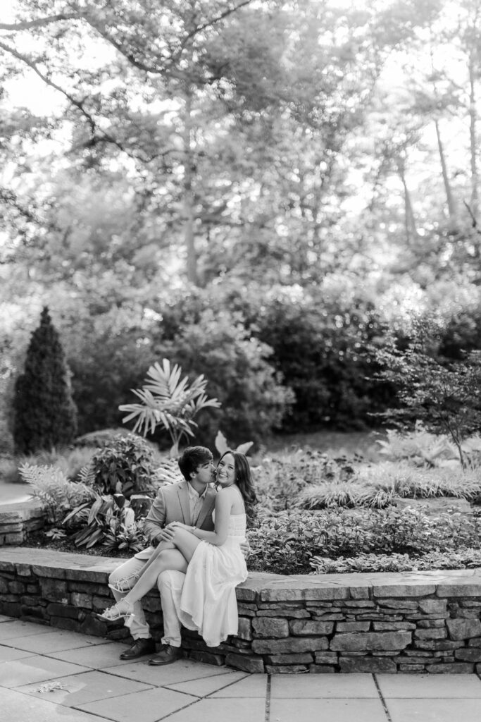 Black-and-white portrait of Brody kissing Emily’s cheek beside a stone garden wall.