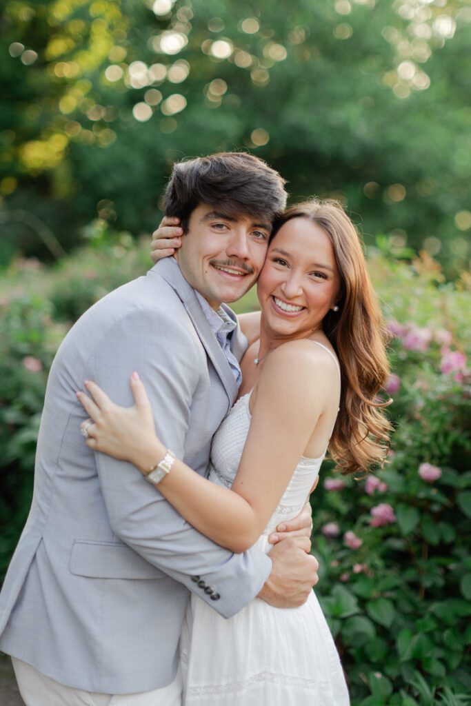 Smiling couple embracing in a flower garden during an outdoor engagement session.