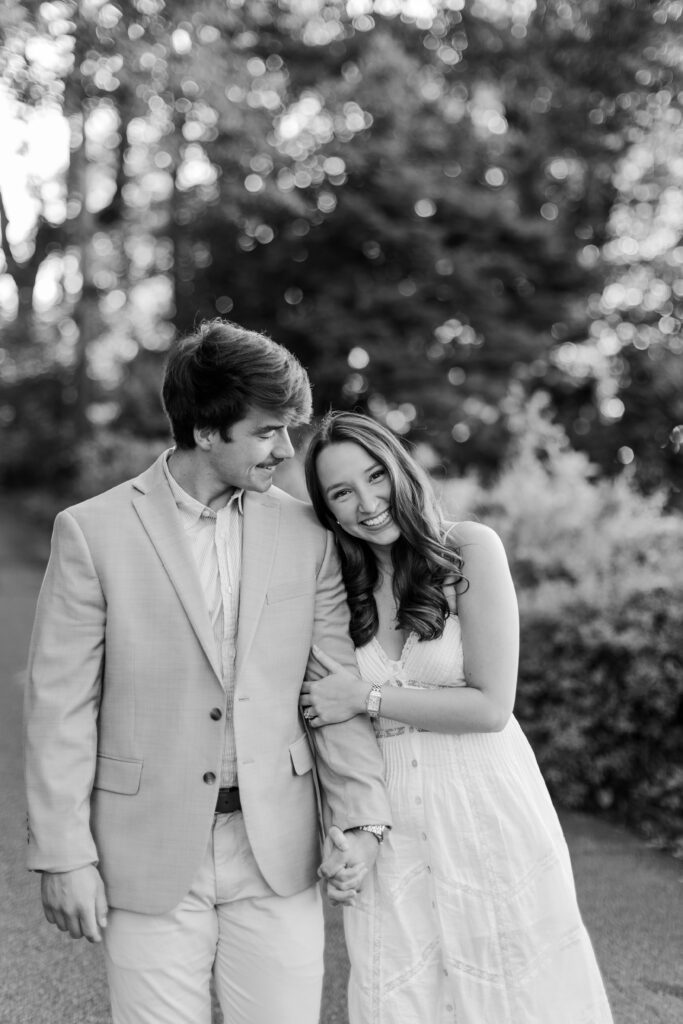 Black-and-white portrait of a couple holding hands and smiling together outdoors.
