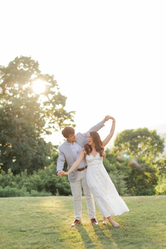 Couple dancing barefoot on a grassy hill in warm golden-hour sunlight.