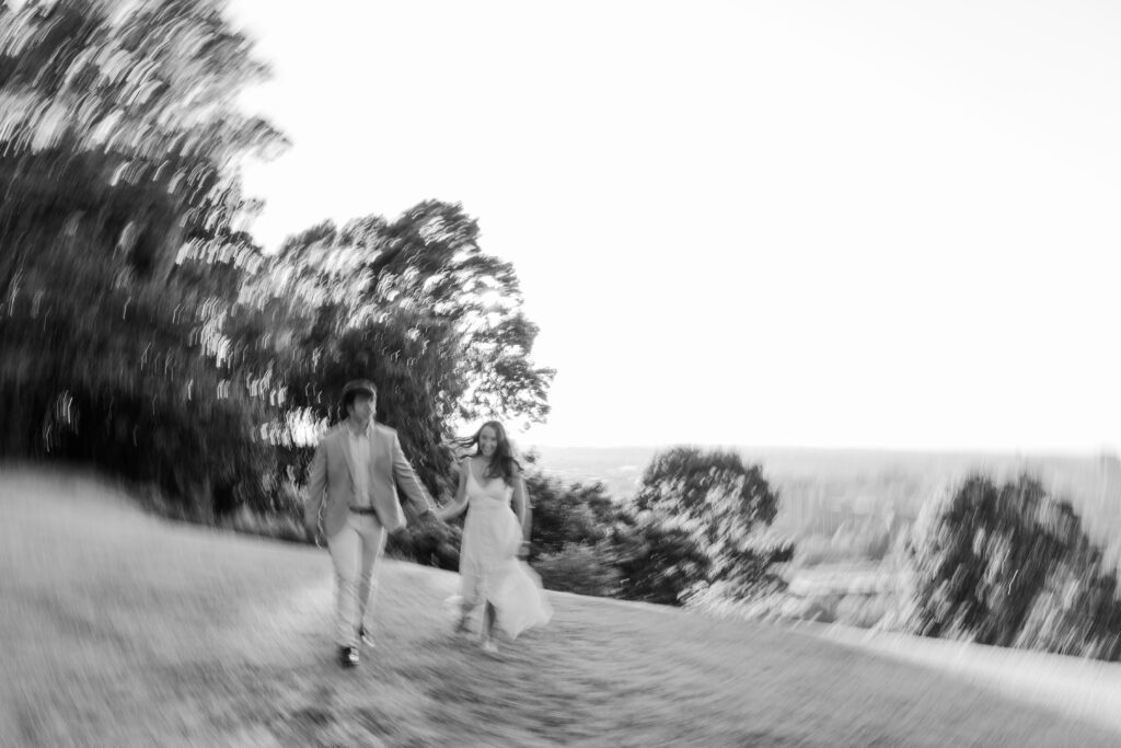 Black-and-white motion blur portrait of a couple running hand in hand across a grassy hill.