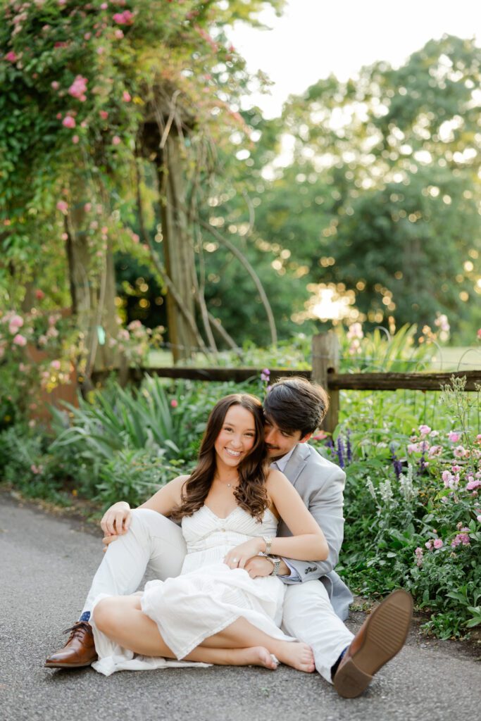 Couple sitting together on a garden path surrounded by colorful flowers and greenery.