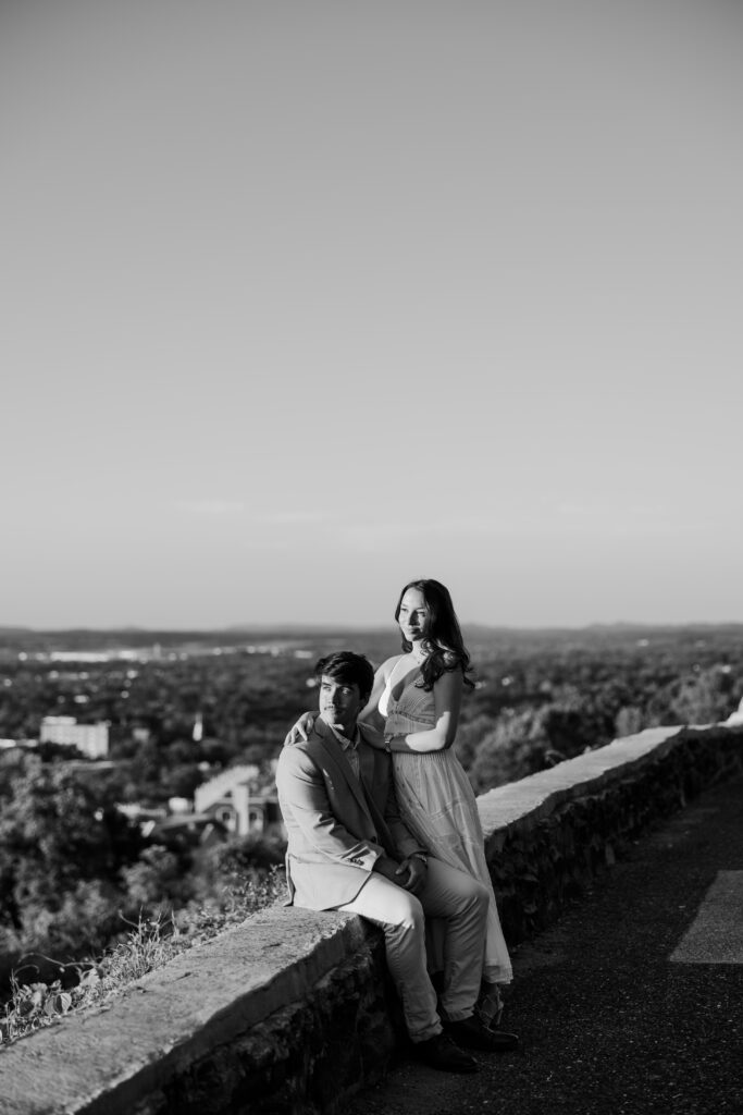 Black-and-white portrait of a couple posing beside a stone overlook with expansive views behind them.