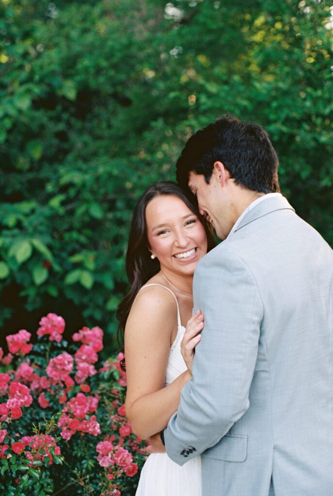 Close-up portrait of a couple embracing beside blooming pink flowers and lush greenery.