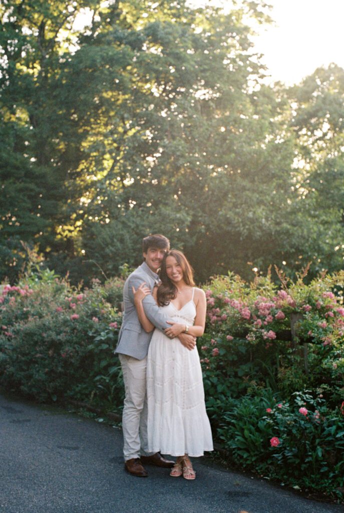 Couple embracing beside blooming pink flowers in a garden during warm evening light.