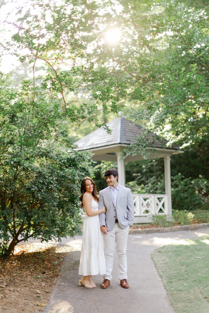 Emily and Brody hold hands on a garden path beside a white gazebo at Birmingham Botanical Gardens.