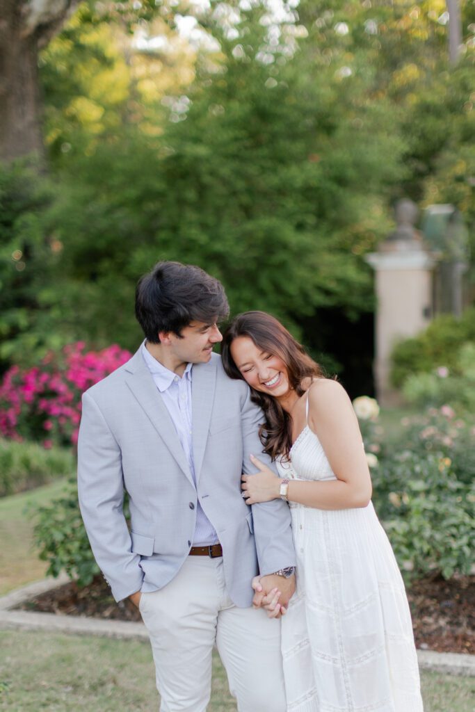 Emily leans against Brody while they hold hands among blooming flowers and greenery.